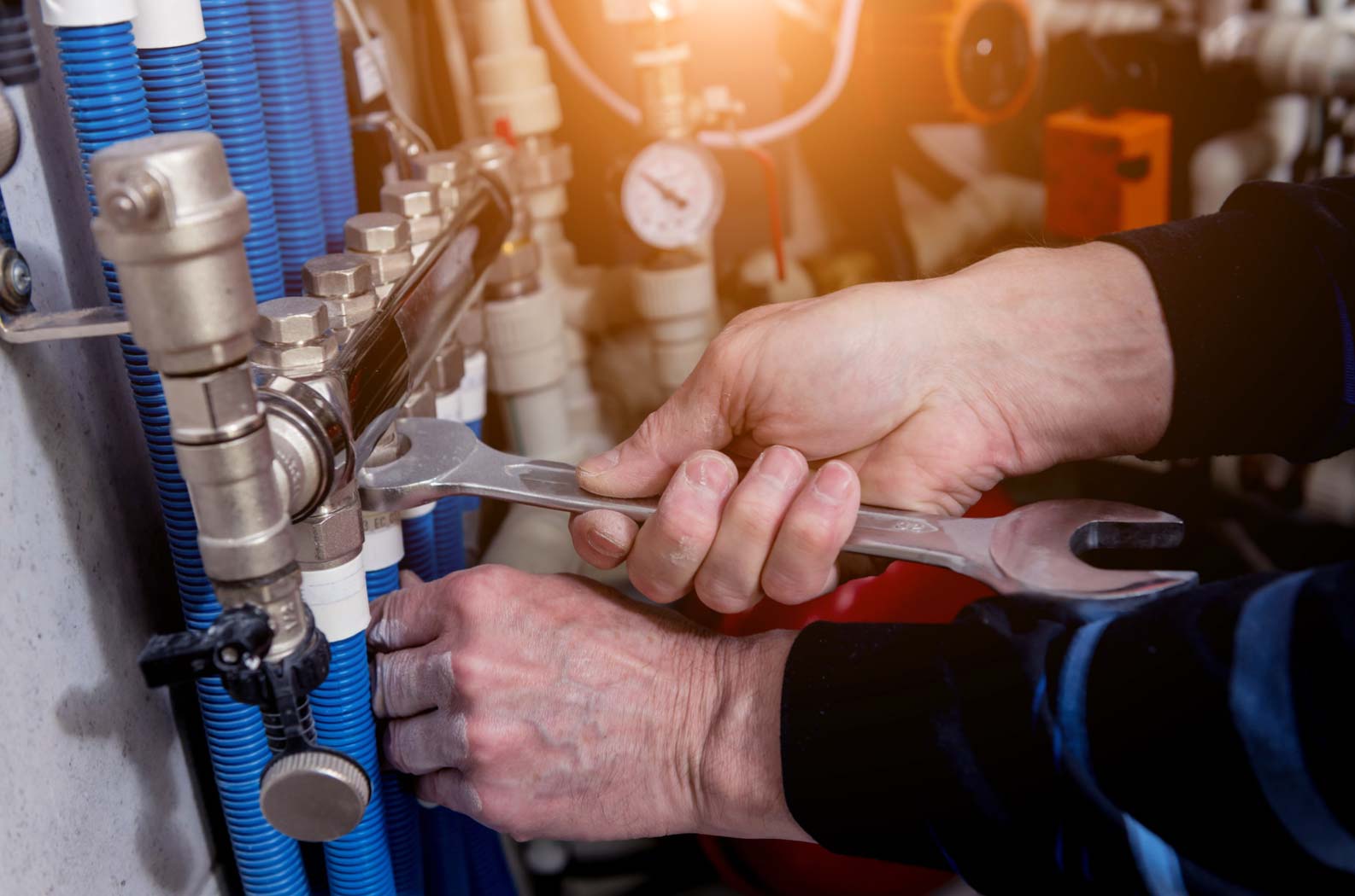 heating system Person using a wrench to tighten a pipe in an industrial setting with blue cables.