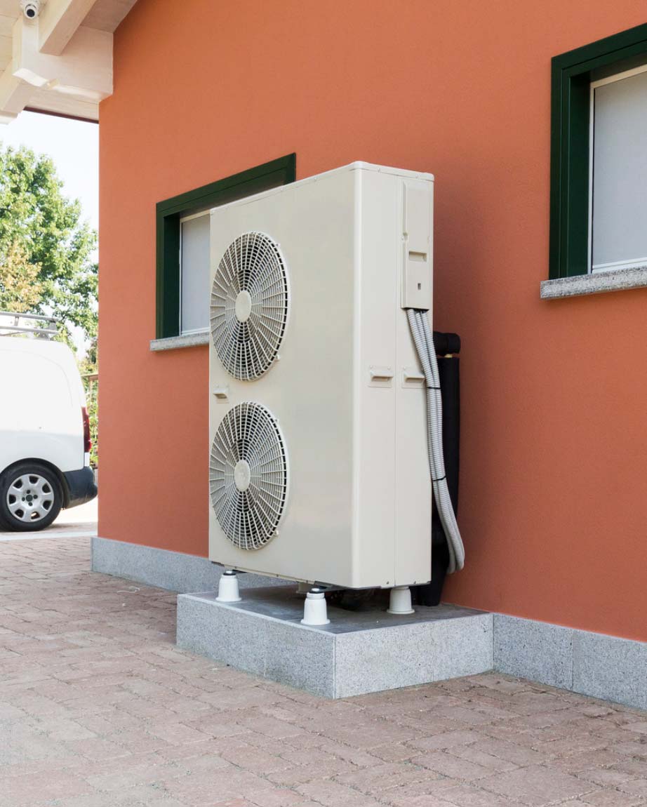 Air conditioning unit with two fans mounted outside an orange building.